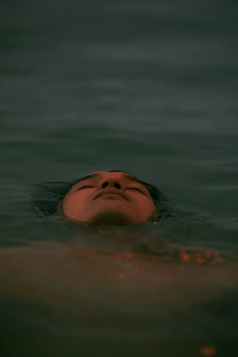 A man floating on his back in still water, eyes closed