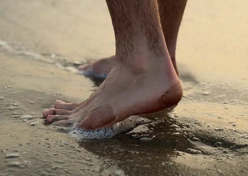 Feet at the water's edge wearing Miracle Bandage patches on the heel and toes