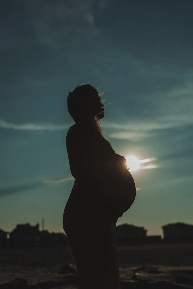 A pregnant woman in silhouette at sunset