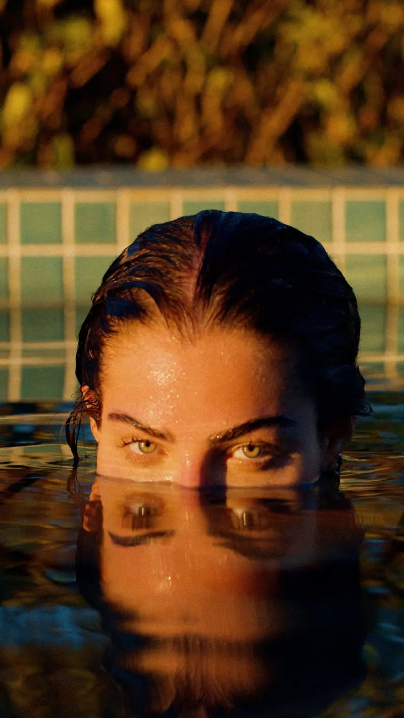 A woman rising from the water at golden hour, eyes just above the surface