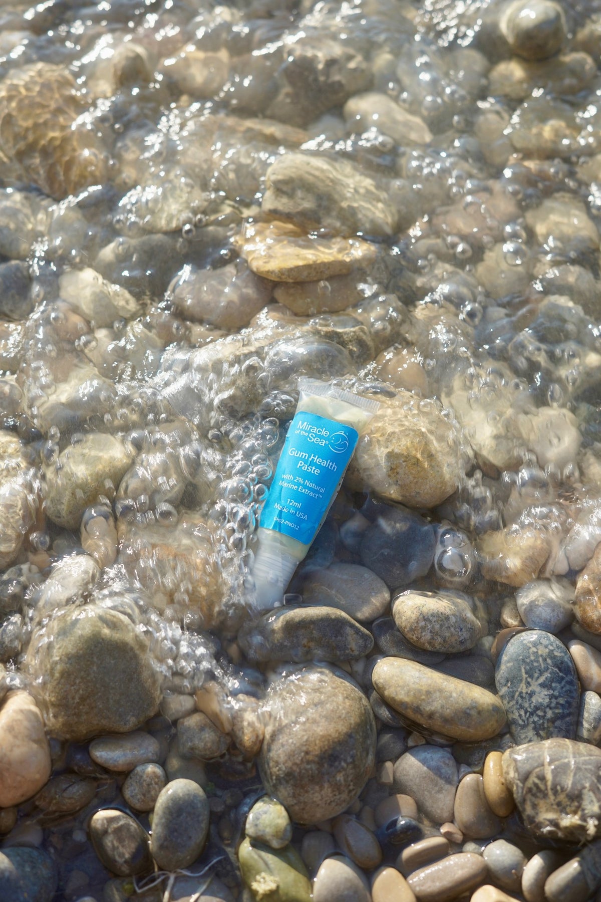 Miracle of the Sea Gum Health Paste tube in shallow water over beach stones